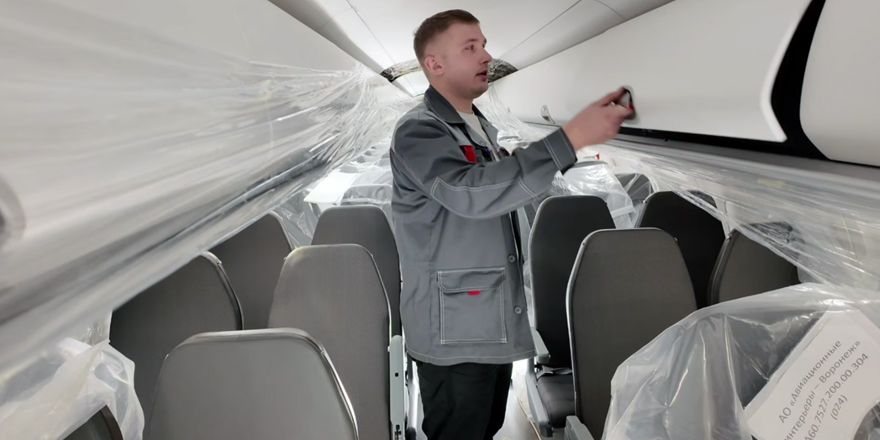 Монтажник проверяет багажную полку, кресла в плёнке